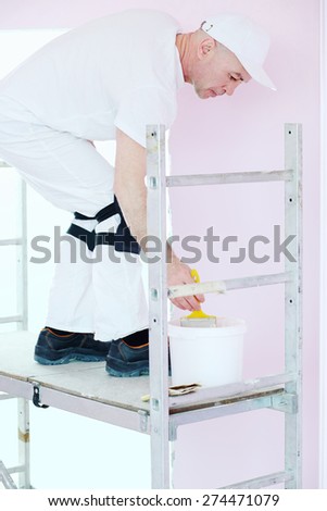 Construction finisher in white clothes with brush and paint stands on scaffolding