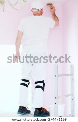 Finisher with brush in hand standing on scaffolding and painting walls near ceiling