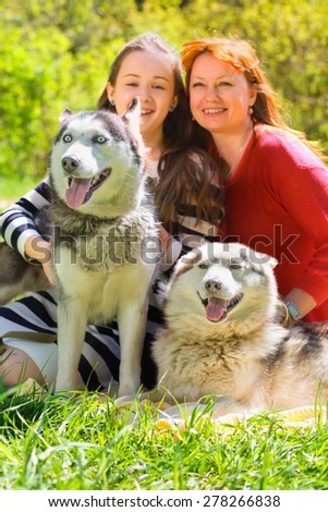 laughing mother and daughter along with two dogs in park on background of green trees, focus on dogs