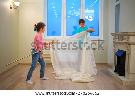 Brother and sister hanging curtains in new apartment in evening