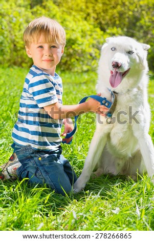 boy in striped T-shirt sitting on grass and holding leash dog in park