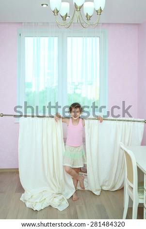 Happy girl holding the curtain with new drapes on the shoulders at the window in the room