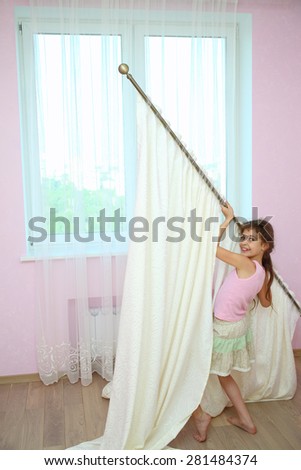 Girl holds the curtain with new draperies at the window in the room