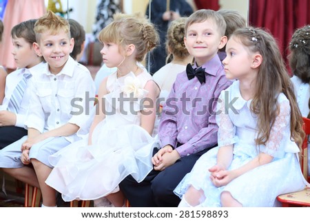 Five elegant small children sit on a chair in the hall at the feast in the kindergarten