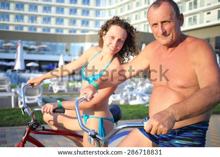 Portrait of elderly man and a young woman in bathing suits on bikes on the hotel in the evening