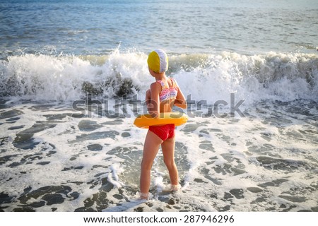 Girl in inflatable ring and a rubber cap in the sea waves