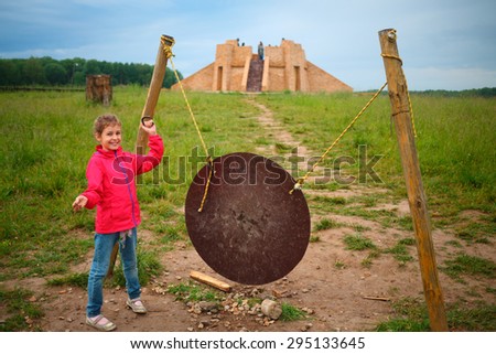 Girl stands near gong and ziggurat in open-air museum at summer