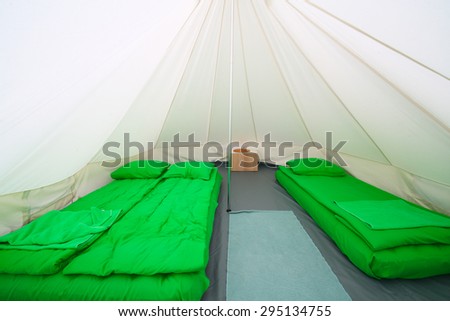Interior white tent for guests with green sleeping bags and inflatable mattresses