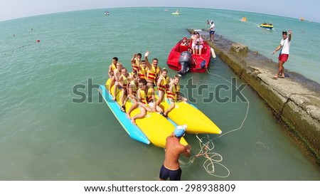 RUSSIA, SOCHI - JUN 20, 2014: People smile and wave hands before ride on inflatable banana at summer sunny day. Aerial view. Photo with noise from action camera.