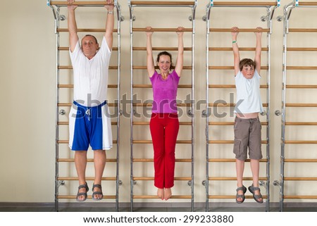 mother son and grandfather hanging on a horizontal bar in a gym