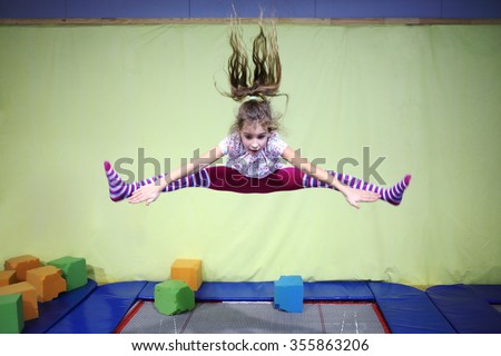 Girl is jumping high in striped tights on the big trampoline.