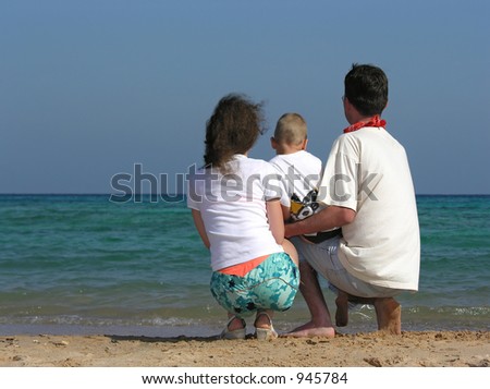 back family of three sit on beach
