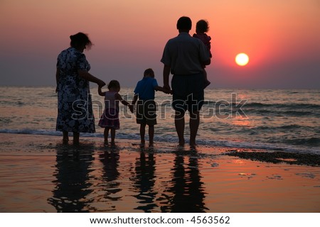Grandfather with grandmother and the children against the background of sunset in waves
