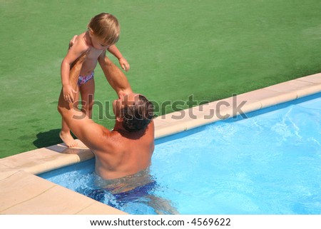 Grandfather standing in pool holds on hands granddaughter