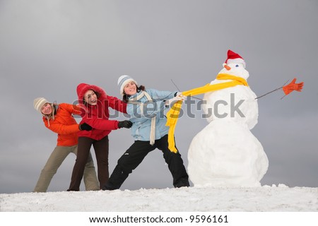 Three young girls pull snowman by yellow scarf
