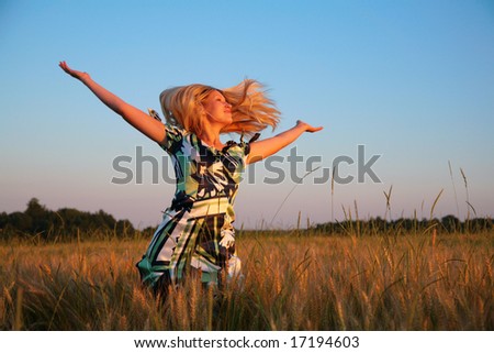 Girl with lifted hands and flying hair on wheaten field