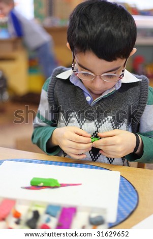 boy with glasses clipart. stock photo : Boy in glasses moulds from plasticine on table