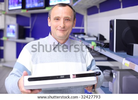 elderly man in shop of radio engineering with dvd-player in hands