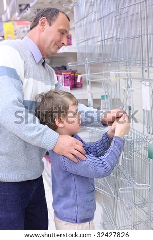 elderly man with boy in store hang grill for roasting on wall