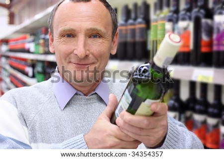 happy elderly man in shop with wine bottle in hands