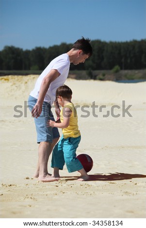 father with son play football on sand
