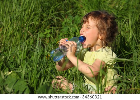girl sits in grass and drinks water from plastic bottle