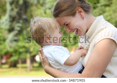 Mother hold baby on hands outdoor in summer and looks on each other