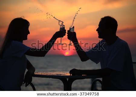 silhouettes of man and woman splash out drink from glass on sea sunset. focus on man