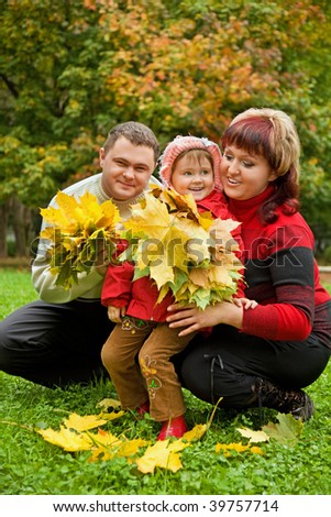 Married couple and little girl collect maple leafs In park in autumn