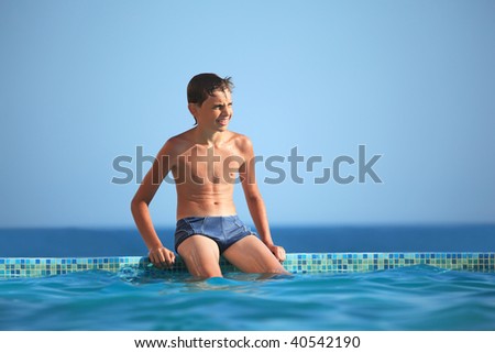 teenager boy wets feet water in pool against sea