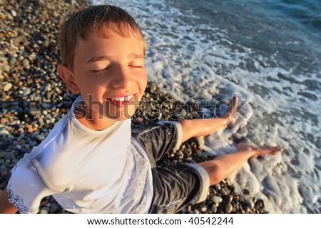 sitting teenager boy on stone seacoast, closed eyes, wets feet in water