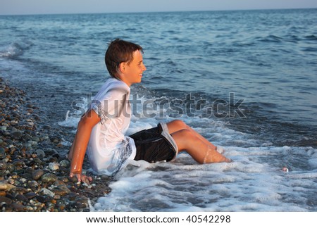 stock photo sitting teenager boy in wet clothes on stone seacoast