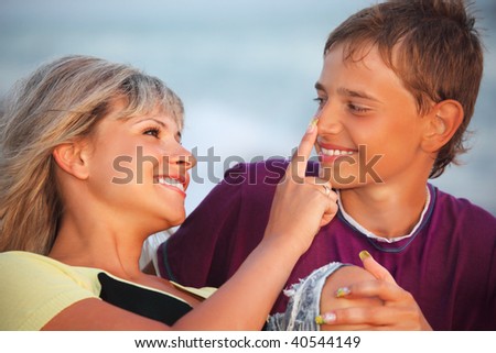 young woman touches with finger nose of smiling boy in evening, Looking against each other