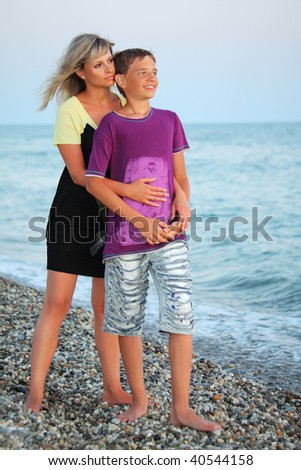young woman embraces smiling boy on beach in evening