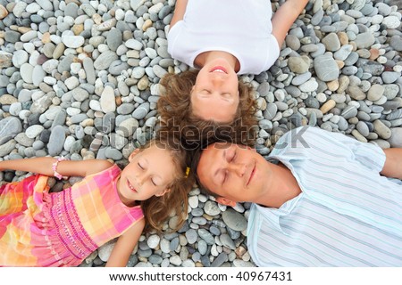 Happy family with little girl lying on stony beach, closed eyes, Concerning with heads
