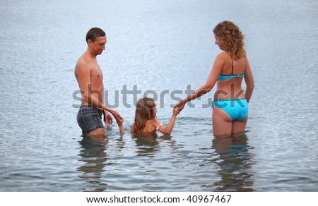 Happy family with little girl bathe in sea, standing back