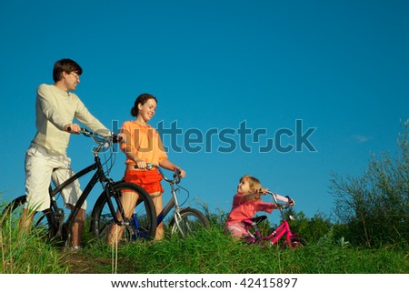 Family from three persons on bicycles. Parents look at a daughter.