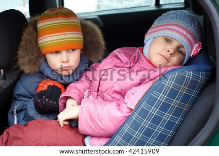 The sad boy with the little girl, in winter clothes in the car.