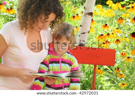 young woman reads the book to little girl in garden