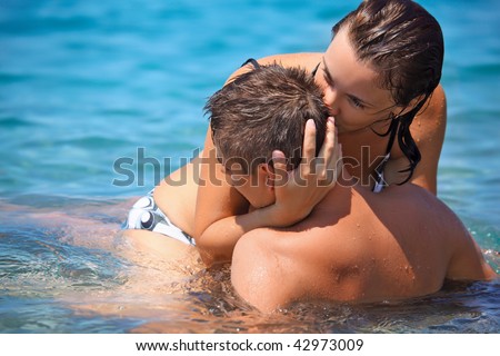 young hot woman sitting astride man in sea near coast, woman kisses man