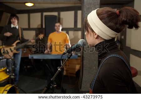 vocalist girl near microphone. focus on head of microphone. electrical guitar player and keyboarder in out of focus