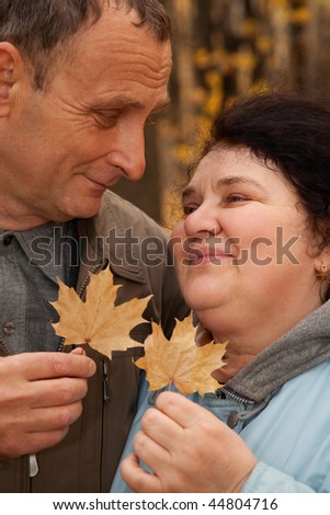 Old man and old woman hold maple leaves and look against each other