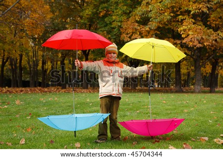 Boy in autumn park. Has control over four multi colored umbrellas.