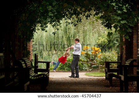 Father and daughter in summer garden  in plant tunnel. Man plays with girl turning her on hands.