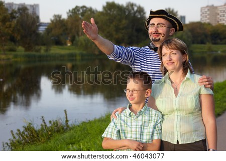 family in fall evening park near pond: man in pirate suit, woman and little boy. man is point away