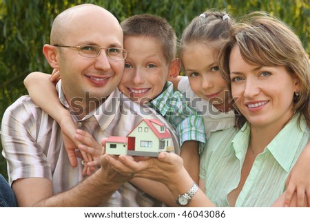 smiling family with two children is keeping wendy house in their hands and looking at camera. focus on boy\'s face. wendy house in out of focus.