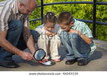 father is using magnifier to burning paper. his son and daughter is looking at this process. focus on left father\'s knee
