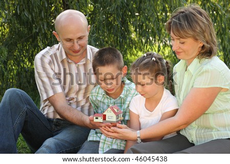 family in early fall park. father, mother, little boy and girl is sitting on the grass near osier and looking at wendy house.