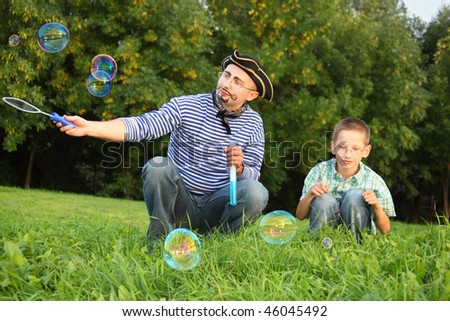 man with drawed beard and whiskers is blowing soap bubbles. his son is looking on little soap bubble.