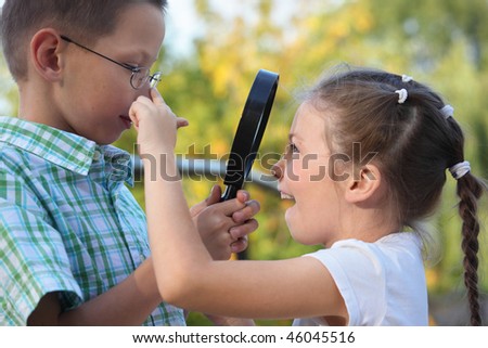children in early fall park. little boy is looking at joyful little girl through magnifier